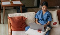 A doctor sitting on the couch on a laptop.
